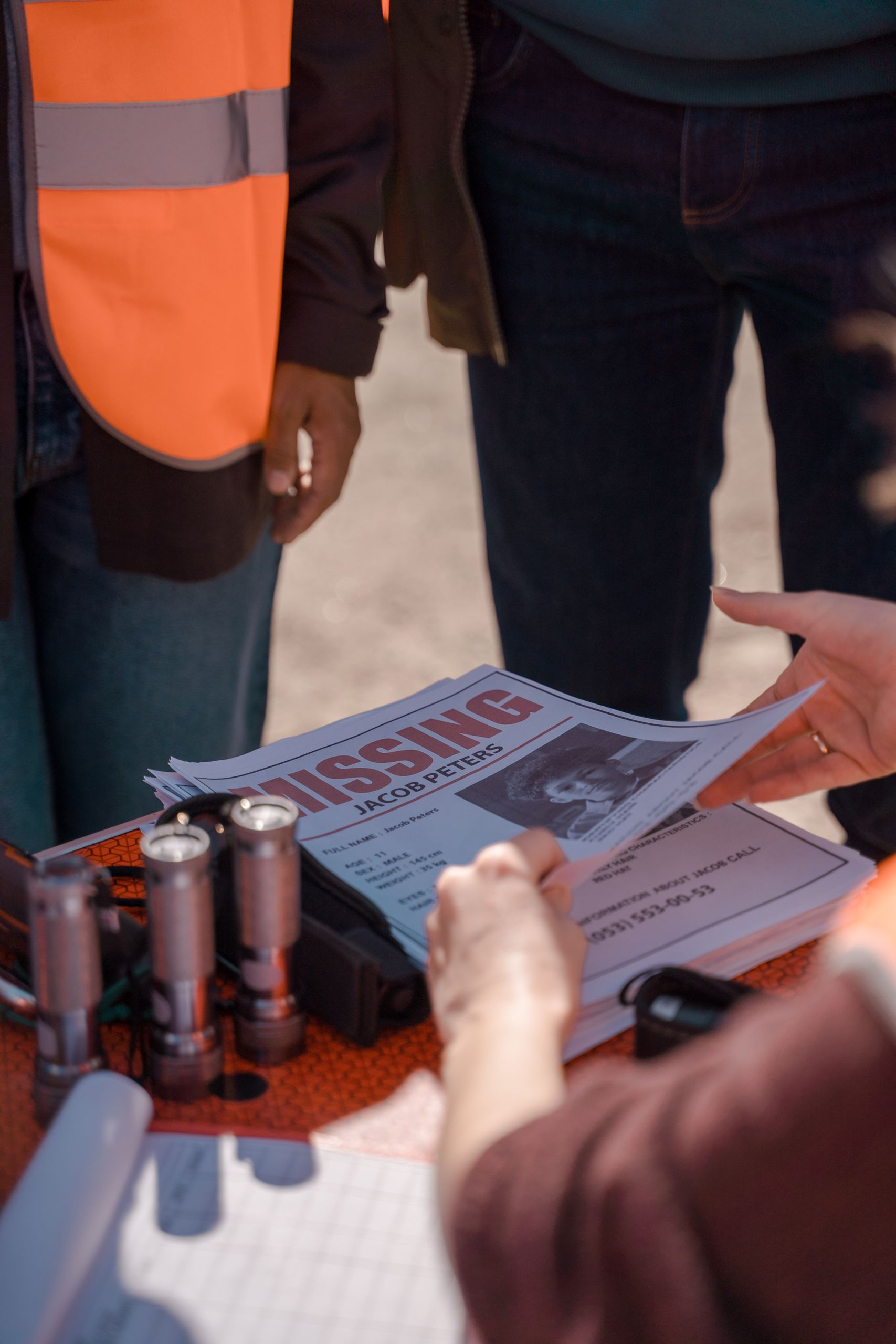 Volunteers organizing during a search effort by examining missing person posters on a sunny day.